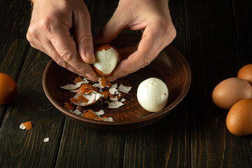 A cook peels a boiled egg from its shell on the kitchen table with his hands. Healthy eggs white...