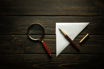 A sheet of paper folded into a triangle with a pen and a magnifying glass on a black desk. Concept...