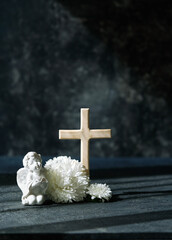 angel baby figurine with white flowers and cross on abstract dark background. concept of faith,...