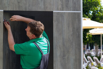 A worker hotel is repairing a locker room near the pool, screwing on a coat hook.