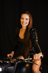 Obraz na płótnie Canvas A woman in a black leather jacket and shorts posing on a motorcycle