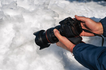 hand of traveler photographer with a modern DSLR camera photographing snow in winter in nature...