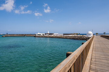 View of the Fermina islet and wooden access bridge. Turquoise blue water. Sky with big white clouds. Seascape. Lanzarote, Canary Islands, Spain.