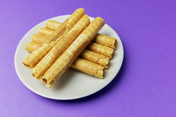 Delicious buttery waffle tubes served on a plate on a purple background
