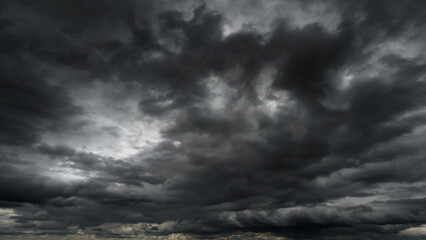 dark dramatic sky with black stormy clouds before rain or snow as abstract background, extreme weather, the sun shines through the clouds, high contrast photo - obrazy, fototapety, plakaty