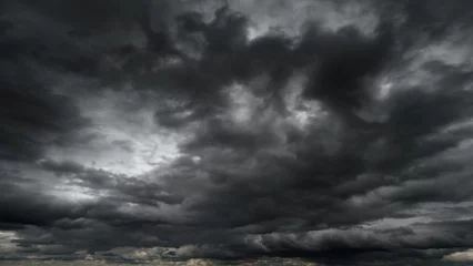 Deurstickers dark dramatic sky with black stormy clouds before rain or snow as abstract background, extreme weather, the sun shines through the clouds, high contrast photo © soleg