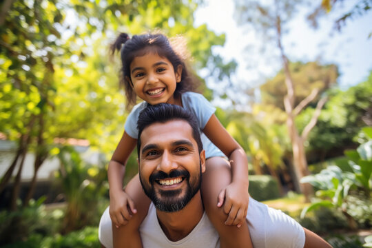 indian little girl sitting on her father's shoulder at park