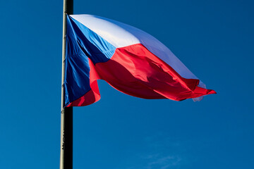 The Czech Republic flag is flying on a flagpole with a blue sky in the background.