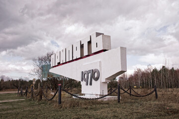 An abandoned structure under a blue sky with scattered clouds. Text in cyrillic: Pripyat, name of...