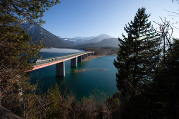 A picturesque bridge spans the tranquil waters, nestled amidst majestic mountains that define the...