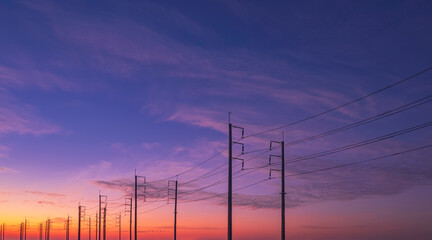 Silhouette two rows of electric poles with cable lines against colorful dramatic twilight sky...