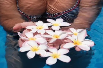 Zelfklevend Fotobehang Young woman in the pool with plumeria (frangipani) flowers. Bali, Indonesia. © Kirill