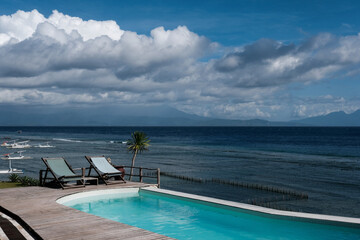 Two lounge chairs by seaside swimming pool on sunny day. Nusa Penida, Indonesia.
