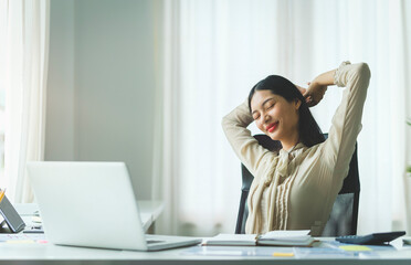 Satisfied asian young woman relaxing at her workplace and looking through the window at office.