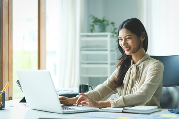 Portrait of happy young woman working on tablet pc while sitting at her working place in office.