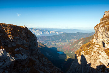 Fototapeta premium Tiny Human Figure of a Woman Tourist Hiker Standing on a Cliff Admiring the Beautiful Environment of European Alps - Mangart Saddle Slovenia - Fusine Lakes Italy