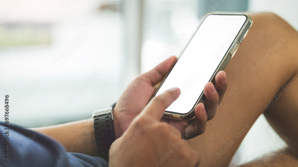 Wall mural cropped image of man lying on couch and using mobile phone. white blank screen for your advertise de