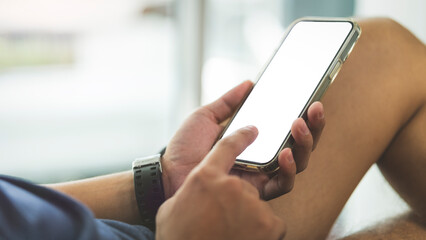 Cropped image of man lying on couch and using mobile phone. White blank screen for your advertise design.