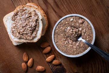 Walnut butter in a bowl with almonds on a wooden background.