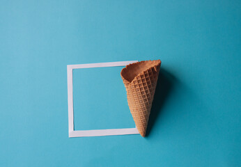 Ice cream cone and paper card frame on blue background. Creative copy space layout. Flat lay pastel...