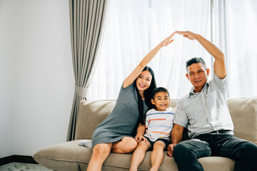 A joyful family seated on a sofa parents forming a roof above their little son. Portraying house insurance children protection and future plans emphasizing family security.