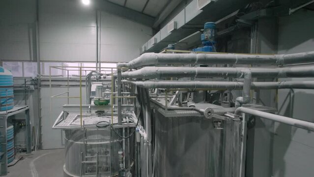 Shiny tanks with chemical materials connected with pipelines in plant workshop. Cistern for distillation at plastic materials production factory