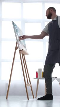 Portrait of an artist working on an abstract painting, using a brush to create a modern painting. Vertical video