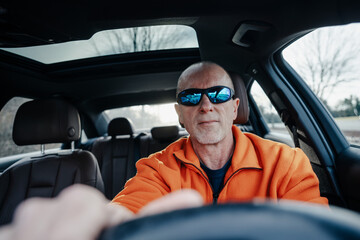 Interior view of an older man with sunglasses driving in a automobile 