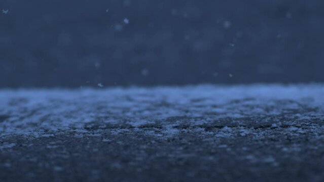 Snowflakes falling into sidewalk street in super slow motion captured at 1000 fps with a high speed camera, car passing by in background