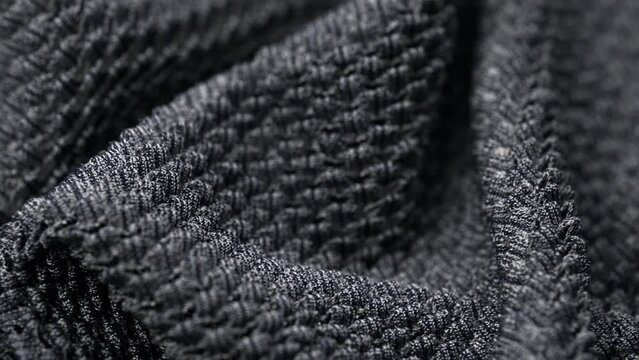 closeup folds rotating knitted textured boucle fabric in dark gray color. convex texture factory fabric. macro. warm and cozy knitwear for cold winter. textile background.
