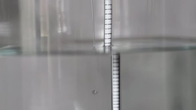 alcohol distilling process closeup - liquid distilled transparent liquid flowing in large glass jar with floating alcoholometer in it.