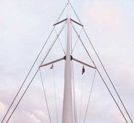Mast of a sailing yacht without a sail. Bottom view on a background of blue sky with clouds.