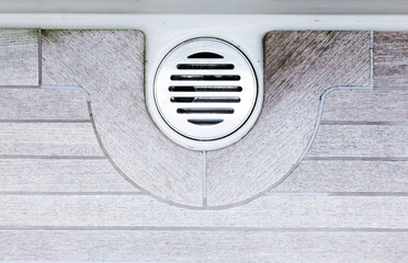 Teak deck of a motor yacht with stainless steel drainage hole, top view.