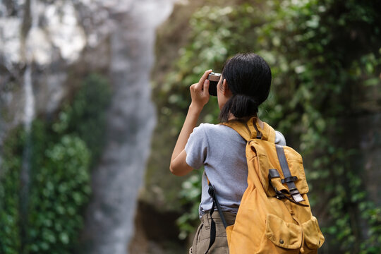 Rear view of female tourist visiting  taking selfie picture in front of waterfall.