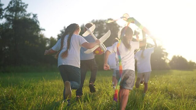 children run through the meadow in the park with toys in their hands. happy family kid dream concept. a group of little kids have fun together and play with flying kites lifestyle toy airplane