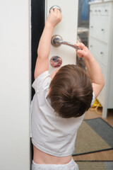 Toddler baby opens the door of the house. A child in a white T-shirt. Kid aged two (two year old)