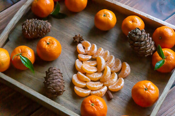Close up of bowl of mandarin oranges on wooden table shot from above. Christmas tree made of...