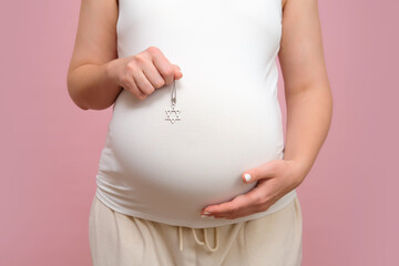 Pregnant woman holding religious Jewish symbol in hand, studio pink background