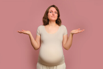 I do not know the gesture of a pregnant woman on a studio pink background. Pregnancy in a woman...