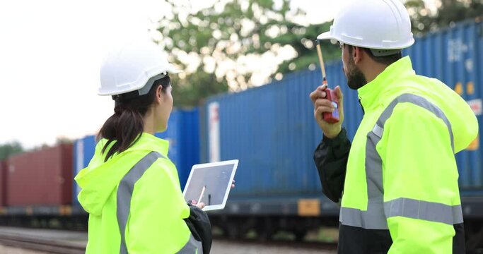 Man and Woman Logistic engineer with green safety jacket and PPE work onsite to control Cargo containers at the train station