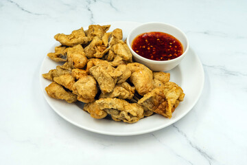 Delicious fried fish meatballs and seasonings with spicy sauce on dish with marble background. Fried meatballs Made from meat. Asian Street Food. Deep fried fish meatballs with sauce on white plate.
