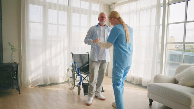 Nurse helps old wheelchair man to drink. Physical therapist woman provides medical help support to senior paralyzed male giving water. Palliative care in late stage of neurodegenerative pathologies.