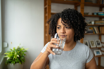 Thoughtful woman drinking water in yoga room at home