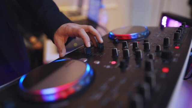 A DJ plays music at a party in a nightclub for a crowd people. DJ control panel for mixing dance music and laptop in a disco club. Hands touching slider buttons, electronic music playing on a mixer.