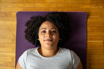 Portrait of woman with afro hairstyle lying on yoga mat at home