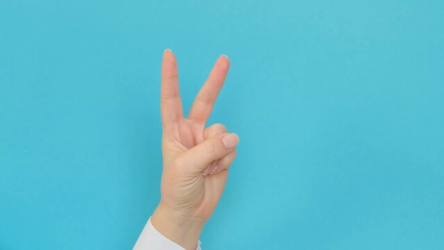 A hand in a white shirt shows the V gesture with two fingers on a blue background. 4k footage