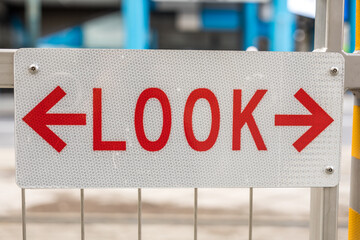 Street sign with “look both ways” on the fence at subway train station