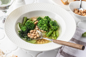 Vegetarian minestrone soup with green vegetables and beans served in white plate and bread on white...