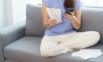 Asian woman holding paper document calculating money savings paying bills in mobile application...