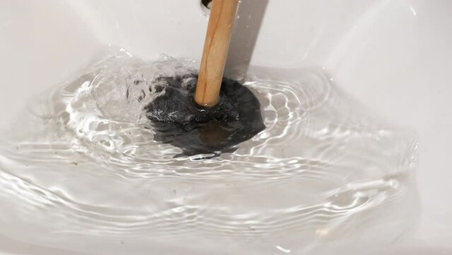 Female cleans a clogged drain with plunger. A view of woman hands with a plunger clean a clogged drain in the bathroom.